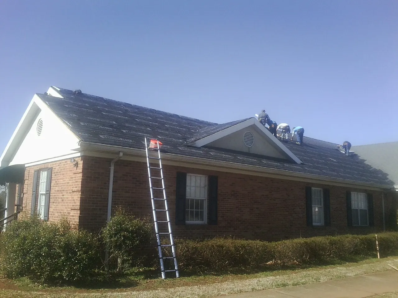 Crew tearing shingles off a brick ranch roof with a ladder set — Emergency Roof Repair work by our crew in Duxbury