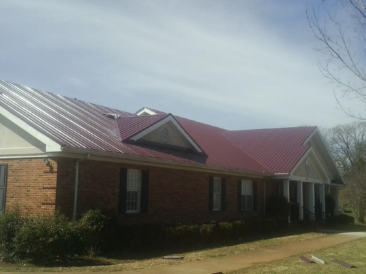 Red metal roof with gabled entries on a long brick building, from a Hail Damage Roof Repair job in Duxbury