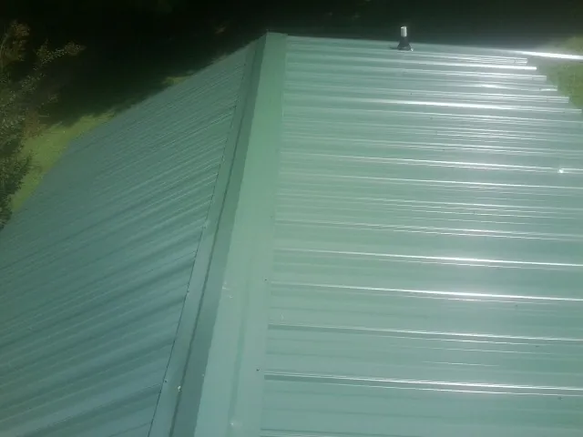 New green metal panels meeting at the ridge of a roof — Flat Roof Repair work by our crew in Duxbury