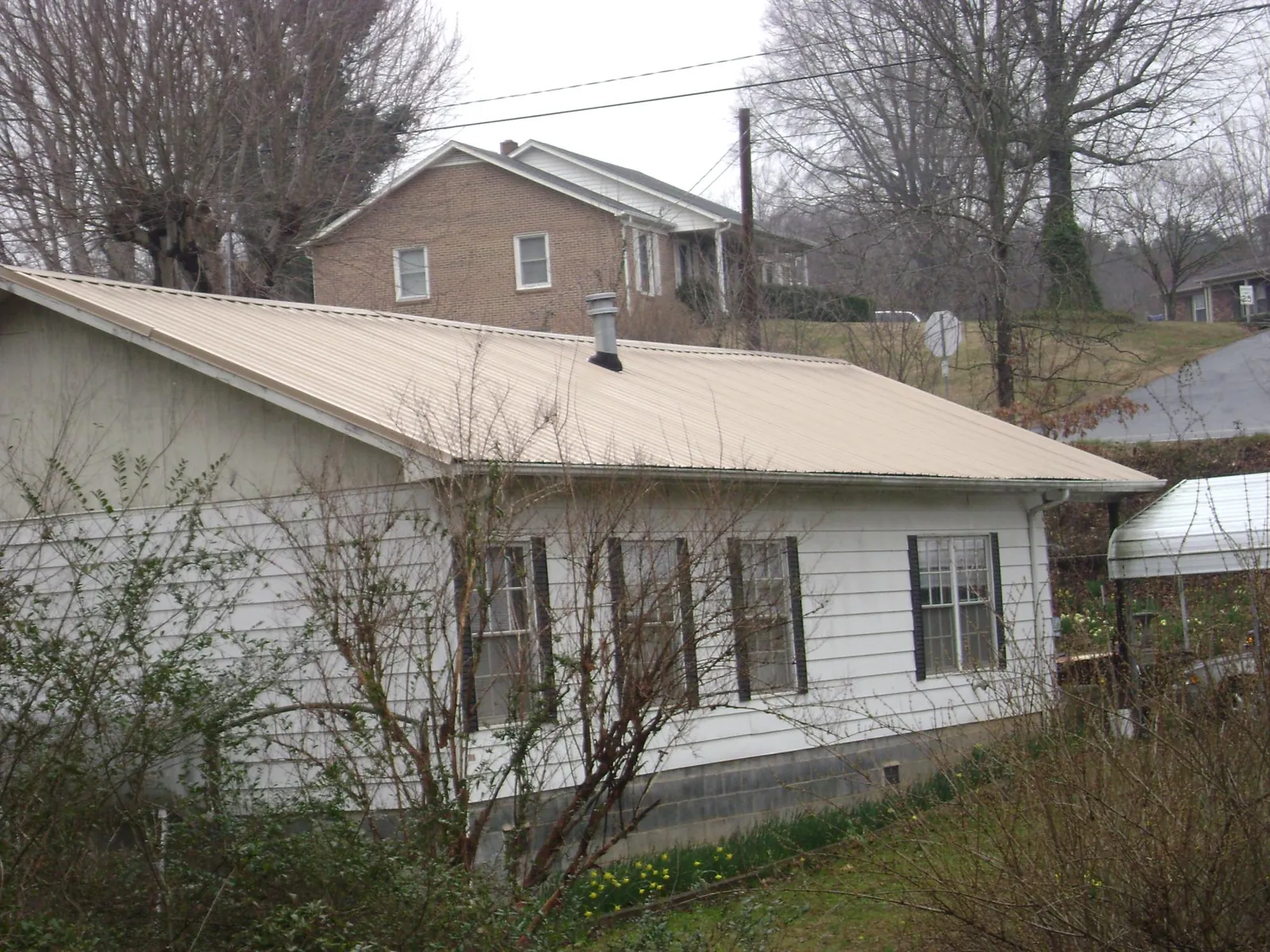 Tan metal roof on a white sided house set into a hillside — Commercial Roofing by Roofing Brothers in Duxbury