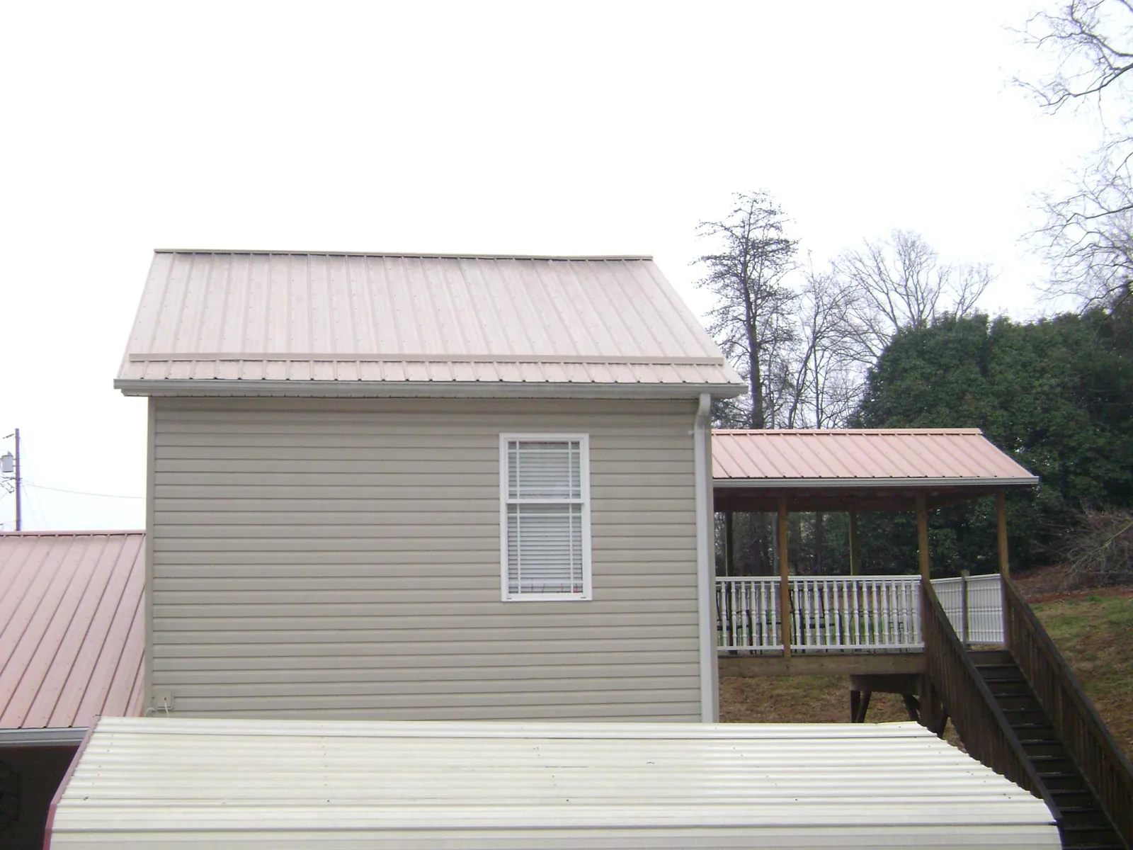Tan metal roofs on a two story addition and attached porch, from a Roof Replacement job in Duxbury
