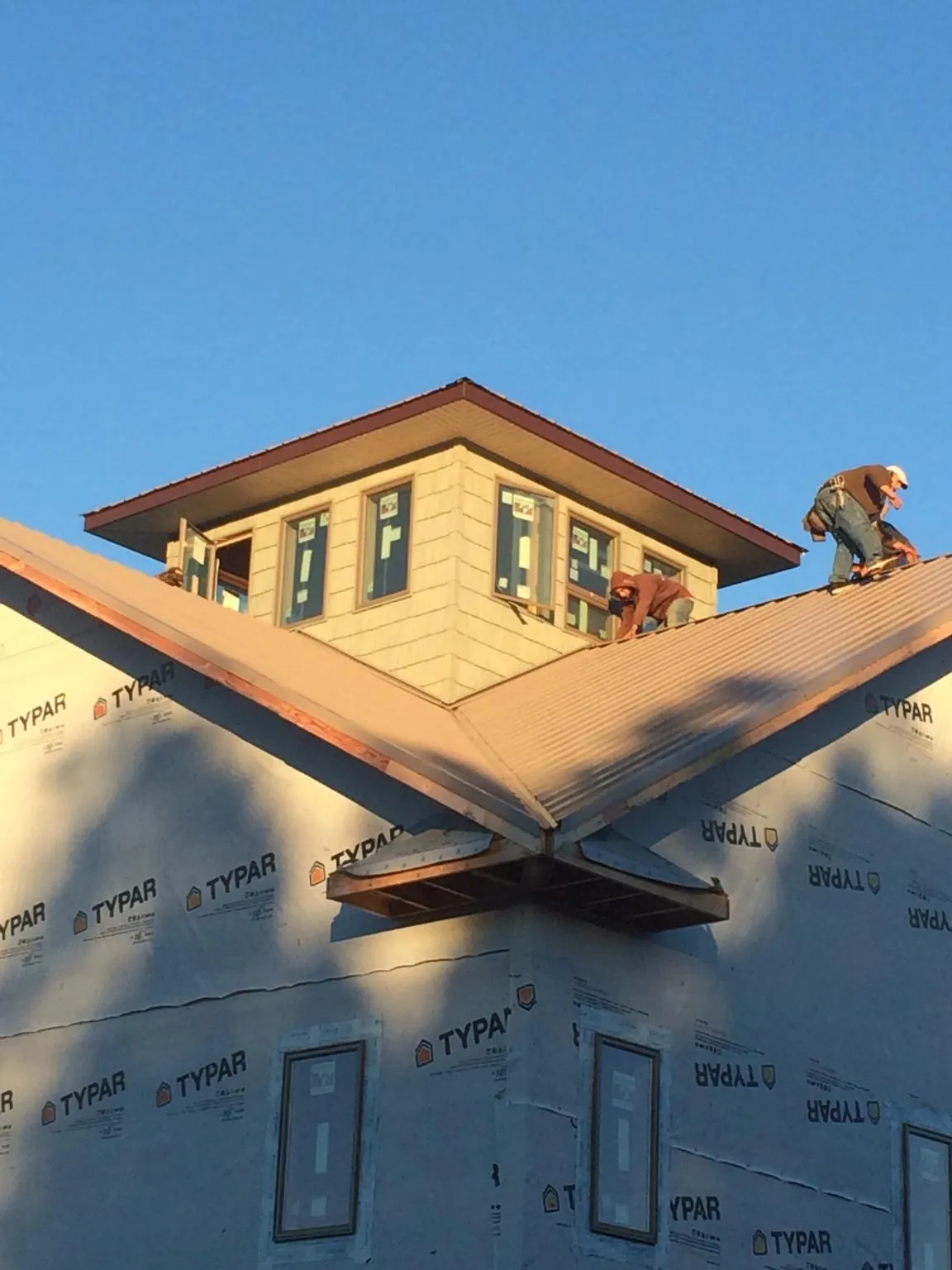 Roofers working around a rooftop cupola on a new metal roof at sunset — Roof Waterproofing in Duxbury by Roofing Brothers